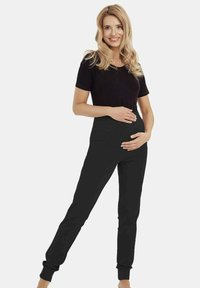 Czarny T-shirt z krótkim rękawem w połączeniu z czarnymi spodniami z wysokim stanem. Strój ma dopasowany krój, odpowiedni dla kobiet w ciąży.