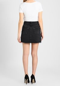 Svart denimminikjol med fransar, två bakfickor och hög midja, kombinerad med en åtsittande vit t-shirt och svarta högklackade skor.