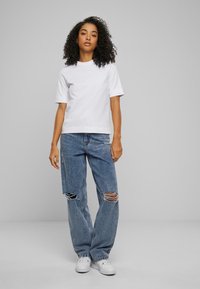 Hvit bomull t-skjorte med korte ermer, kombinert med lyseblå slitte jeans. Modell iført hvite sneakers. Enkel, uformell stil.