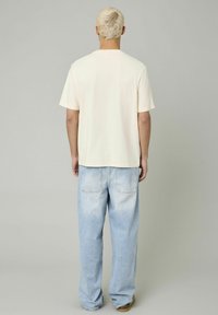 T-shirt crème à manches courtes associé à un jean à coupe décontractée et délavé. Le t-shirt a une coupe droite ; le jean présente un design classique à cinq poches.