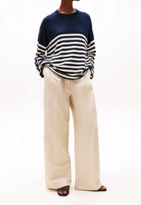 Navy- und weiß gestreifte Langarmbluse, lockere Passform, mit lockeren beigen Hosen und schwarzen Sandalen. Leichte Stoffe, lässige Silhouette, minimale Details.