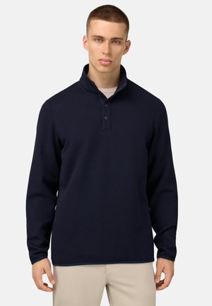 Pull-over bleu marine avec un col, tissu texturé, patte de boutonnage et manches longues. Positionné sur un fond neutre.