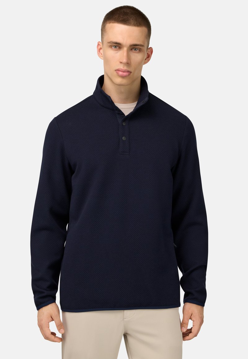 Jūras flotes kreklis ar apkakli, teksturēts audums, poga plaukts un garas piedurknes. Novietots uz neitrāla fona.