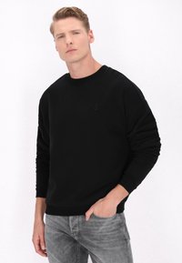 Sort crew neck sweatshirt i blødt stof, med lange ærmer og en diskret logo detalje. Kombinationen med lysegrå jeans.