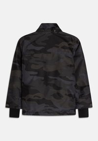 Svart kamouflagemönstrad jacka med hög krage, tryckknappar och elastiska ärmmuddar. Tyget har en slät textur med en subtil lyster.