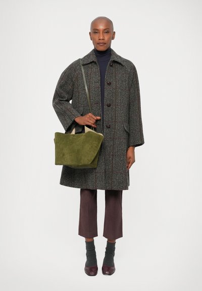 Manteau en laine à carreaux gris avec de gros boutons, associé à un pantalon bordeaux, des chaussettes grises et des chaussures bordeaux. Porte un sac en daim vert olive.
