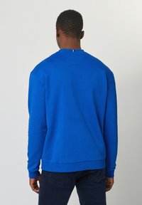 Sudadera azul de manga larga, con cuello redondo, puños y dobladillo acanalados. Textura suave y color sólido, diseño minimalista. Vista desde la parte posterior.