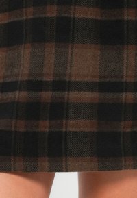 Braun- und schwarzkariertes Gewebe mit strukturiertem Finish, das große Quadrate und ein weiches Aussehen aufweist; die Kanten sind gerade und sauber.