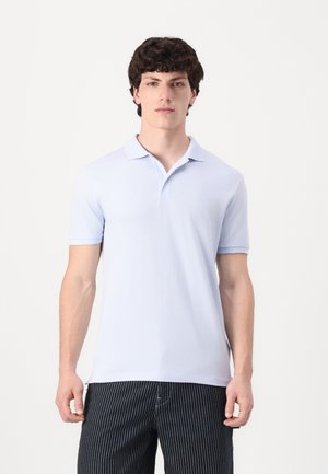 Polo shirt bleu clair à manches courtes, en coton doux, avec un col et une coupe droite. Associé à un pantalon noir à rayures.