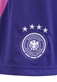 Jersey deportivo de tela morada con un emblema bordado circular en blanco que presenta un águila, el texto "DEUTSCHER FUSSBALL-BUND" y cuatro estrellas arriba.