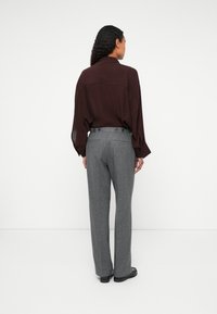Camisa larga de manga larga en marrón con un corte holgado, combinada con pantalones grises ajustados que presentan una textura suave y cuatro botones visibles en la cintura.