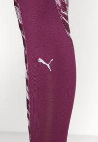 Leggings color marsala con un design strutturato, caratterizzati da un logo Puma bianco. Il tessuto è liscio ed elastico, ideale per l'abbigliamento sportivo.