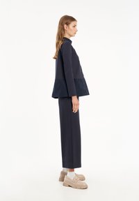 Completo due pezzi color navy composto da una maglietta a maniche lunghe con orlo a peplo e pantaloni dritti coordinati, abbinato a calzature di colore chiaro.