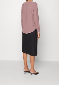 Blusa a maniche lunghe di un delicato rosa, con orlo arrotondato e piega sul retro, abbinata a una gonna midi nera a pieghe e sandali neri open-toe.