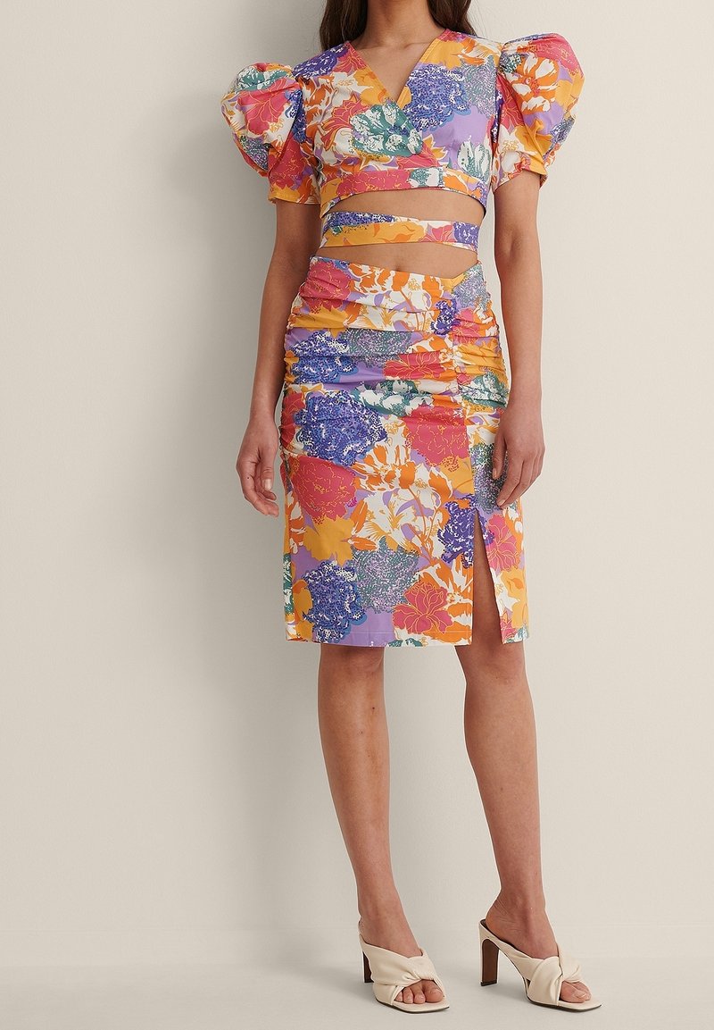 To-delt blomsteroutfit med en cropped top med puffærmer og en rynket nederdel med slids, i levende farver som orange, lilla og grøn.
