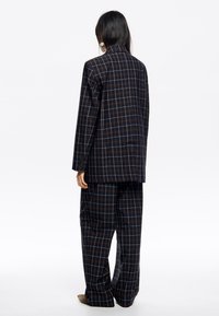Czarna kratowana marynarka z dopasowanymi spodniami. Wykonana z tkaniny o delikatnym wzorze w drobną kratkę w odcieniach ciemnoniebieskiego i brązowego. Luźny fason.