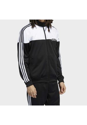 Chándal adidas en blanco y negro con cremallera frontal, con tres franjas blancas a lo largo de cada manga y en los laterales del pantalón. Textura de tejido suave.
