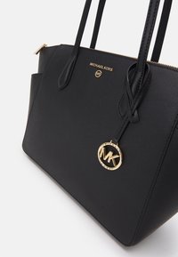 Zwarte gestructureerde tote bag van textuursynthetisch materiaal met twee handvatten, gouden hardware, reliëflogo en ritsluiting.