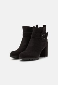 Botas de tobillo de ante negro con un tacón grueso. Presentan una correa trenzada con un detalle de hebilla. Cuero texturizado con un acabado suave.