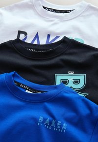 Kolm t-särki valget, musta ja sinist värvi. Igal t-särgil on kiri "BAKER by TED BAKER." Mustal särgil on sinine graafiline disain.