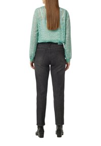 Durchsichtige, mintgrüne Bluse mit strukturiertem Muster und elastischen Bündchen, kombiniert mit dunklen Jeanshosen und schwarzen Ankle Boots.