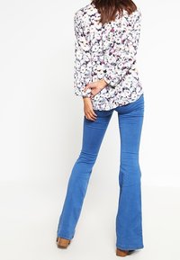 Blouse à motif floral avec manches longues, associée à un jean évasé bleu. Le jean est uni, avec une texture lisse et une coupe ajustée.