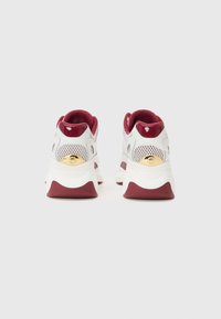 Scarpe sportive bianche e bordeaux con una tomaia in rete testurizzata, collo imbottito e un accento dorato lucido sul tallone. Suola intermedia bianca spessa.