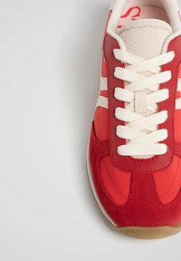 Baskets rouges avec une tige en cuir texturé et suède, des lacets crème et une semelle beige. Présentent des détails de couture et un design à bout rond.