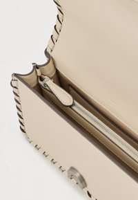 Beige bőrtáska fonott szélekkel, cipzáras rekesszel és fém kiegészítőkkel. Simább tapintás és minimalista dizájn finom logózással.