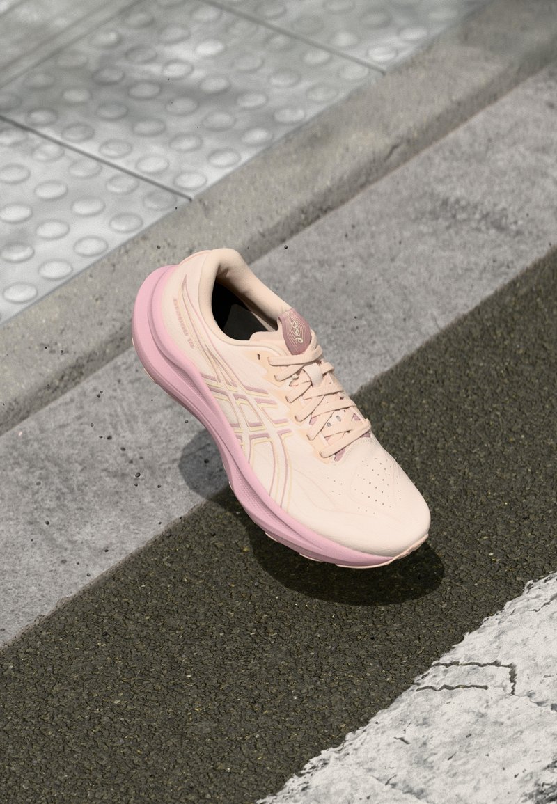 Helles rosa Sport Schuhwerk mit einem glatten synthetischen Obermaterial, atmungsaktiven Perforationen und einer gepolsterten Sohle mit einem leichten rosa Akzent.