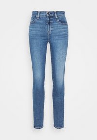 Jeans ajustados en denim azul medio, con un diseño clásico de cinco bolsillos, cremallera y un sutil desgastado a lo largo de los muslos y las rodillas.