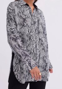 Long-sleeve button-up blouse in black and white featuring a varied pattern of dots and shapes, with a collared neck and side slits.