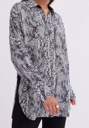 Langdurige blouse met lange mouwen in zwart en wit, met een gevarieerd patroon van stippen en vormen, voorzien van een kraag en zijsplitten.