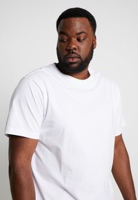T-shirt en coton blanc avec un col rond, des manches courtes et une coupe décontractée, caractérisé par une texture lisse et uniforme, sans motifs ni graphiques visibles.