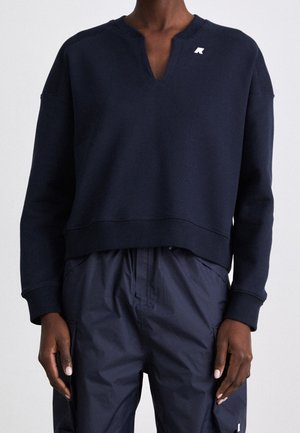 Personne portant une chemise bleu marine foncé à manches longues avec un petit logo blanc près de l'encolure et un pantalon assorti bleu marine.