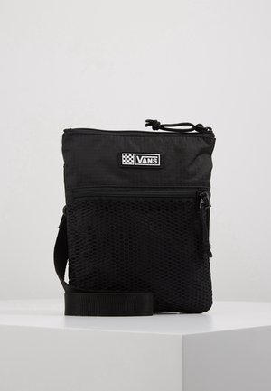 Petit sac bandoulière noir Vans avec sangle réglable, poche avant zippée en mesh et fermeture éclair sur le dessus, présenté sur une surface blanche.