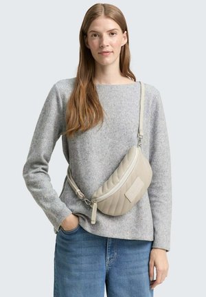 Borsa a tracolla beige trapuntata con chiusura a zip e una patch in pelle. Indossata sopra un maglione grigio con tessuto testurizzato.