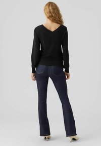 Maglione nero intrecciato con scollo a V e maniche lunghe, abbinato a jeans svasati blu scuro con tasche posteriori e cuciture sottili, indossato con tacchi.