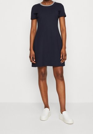 Vestido corto de manga corta en color navy con un diseño ajustado y un cuello redondo con ribete blanco; combinado con zapatos blancos sin cordones.