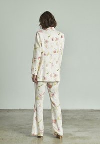 Conjunto de dos piezas con estampado floral en tejido ligero. La chaqueta cuenta con botones y un corte entallado; pantalones de campana con un patrón similar. Colores suaves y pastel.