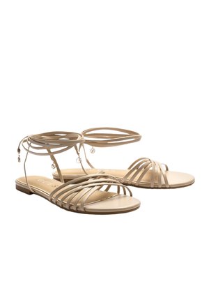 Sandales plates beige avec plusieurs fines lanières sur les orteils et des liens à nouer autour de la cheville ornés de petits charms décoratifs.