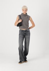 Grijze mouwloze coltrui, high-waisted grijze jeans en zwarte sneakers met een gumrubberen zool; kleine zwarte handtas, minimalistisch ontwerp.