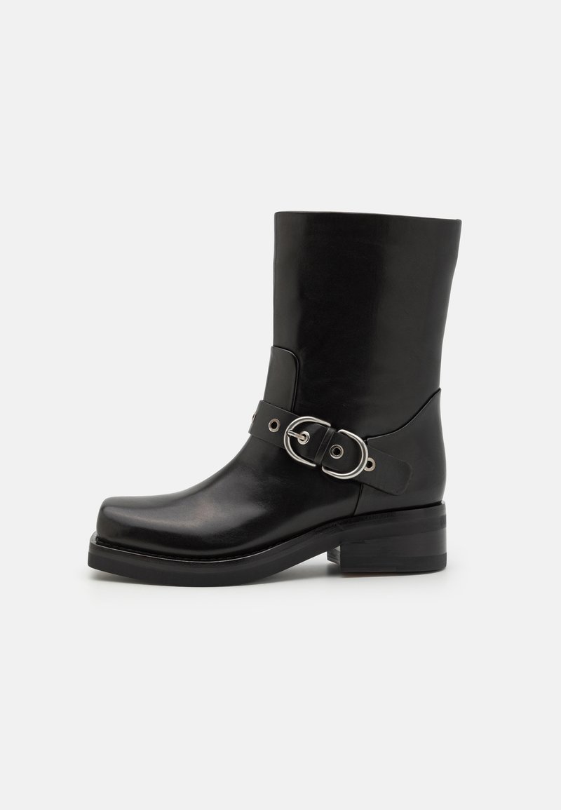 Bottines en cuir noir avec un tige cylindrique, un détail de bride à boucle métallique, un bout rond et un petit talon bloc. Texture lisse.