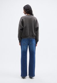 Γκρι φαρδιά φούτερ με ώμους σε χαμηλή θέση, σε συνδυασμό με τζιν παντελόνι ψηλόμεσο, με φαρδιά μπατζάκια σε μπλε χρώμα με ξεβαμμένη υφή και πίσω τσέπες.