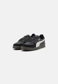 Sapatos atléticos pretos e cinzas com um cabedal em camurça e couro texturizado, com detalhes em branco, perfurações e sola de borracha.