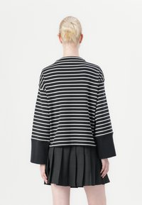 Blusa de mangas longas listrada em preto e branco com mangas largas, combinada com uma saia plissada preta. O tecido parece macio e texturizado.