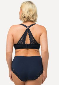 Bralette in pizzo blu navy con design triangolare e spalline incrociate, abbinata a slip a vita alta coordinati con dettagli in pizzo.