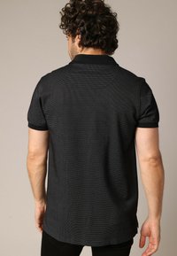 Polo-shirt noir avec un motif texturé, à manches courtes et un col classique. Présente un design subtil et un ourlet droit.