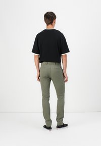 T-shirt noir à manches courtes avec des accents blancs, associé à un pantalon slim vert olive et des chaussures de skate noires, vu de dos.