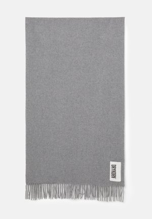 Écharpe en laine gris clair unie avec des extrémités à franges et une étiquette rectangulaire blanche affichant le nom de la marque "DRYKORN" en lettres noires.